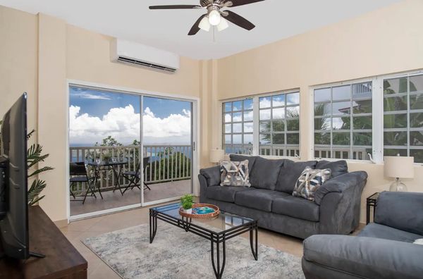 Cozy living room with gray sofas and a balcony overlooking a scenic ocean view.