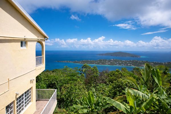 Coastal view from a beige house overlooking lush greenery and islands in the ocean.