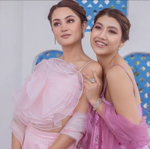 Two women in elegant pastel pink dresses posing together.