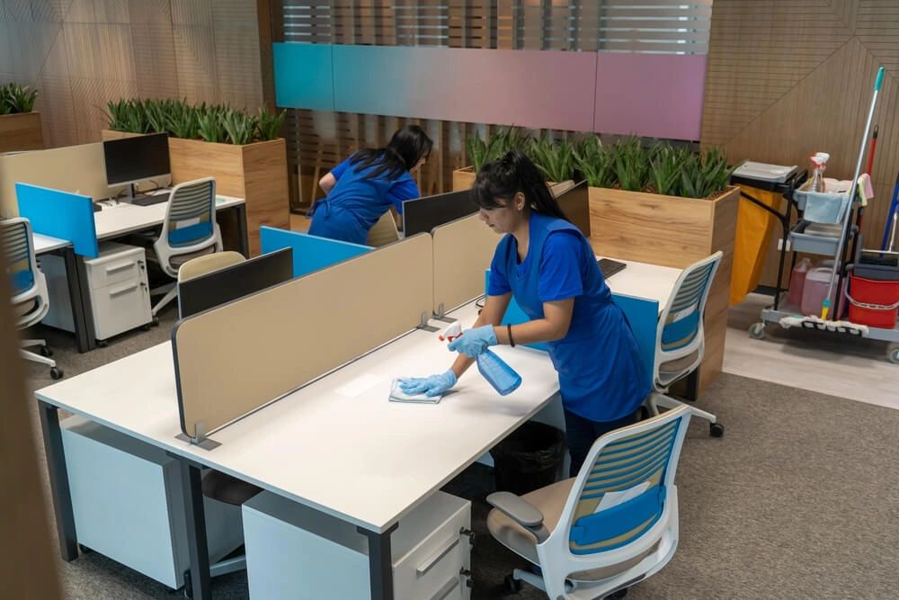 Cleaning ladies clean desks in an empty office space