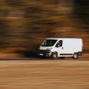 A white van speeding along a road with a blurred autumn background.