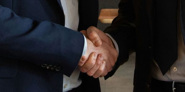 Two individuals in suits shaking hands in a business setting.