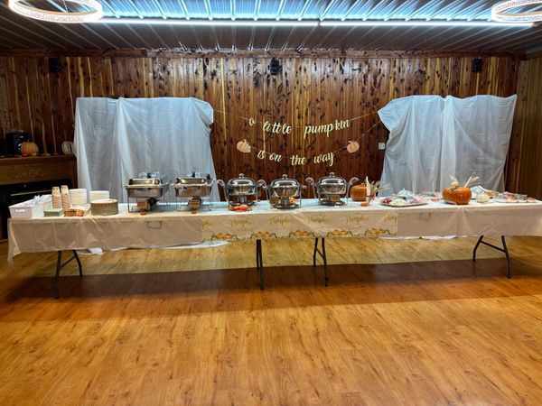 A buffet table with food and a "a little pumpkin is on the way" sign on a wooden wall.