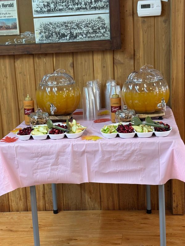 A table setup with fruit punch dispensers, fresh fruit, and syrup bottles.