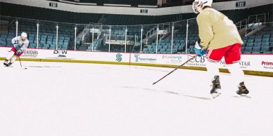 Two hockey players in an empty arena practicing shots.