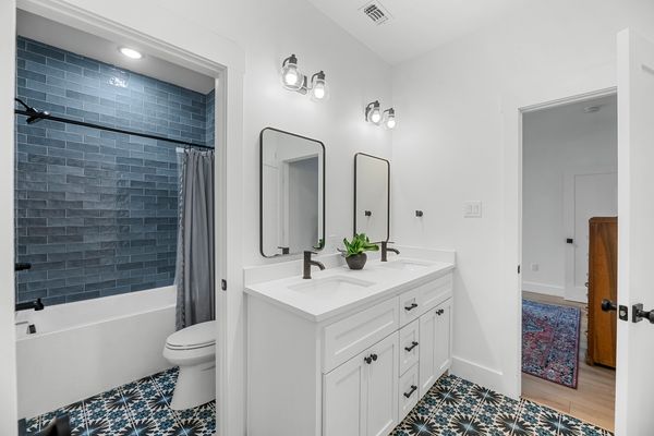 Modern bathroom with white vanity, dual mirrors, and patterned floor tiles.