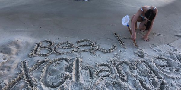 A girl drawing in the sand with a net on the beach at sunset.