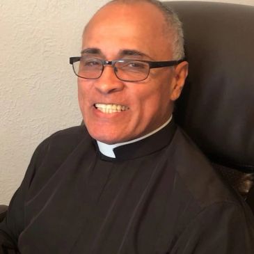 Smiling man wearing glasses and a clerical collar.