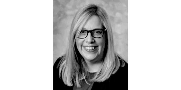 Smiling woman with glasses and long blonde hair in a black and white portrait.