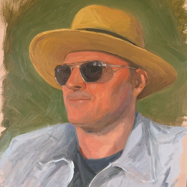 Portrait of a man wearing a yellow hat and sunglasses against a green background.