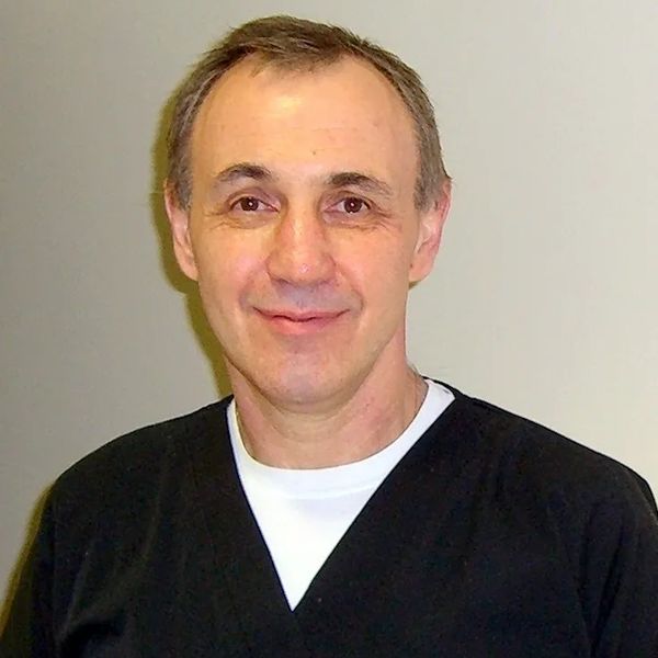 A middle-aged man smiling gently at the camera against a plain background.