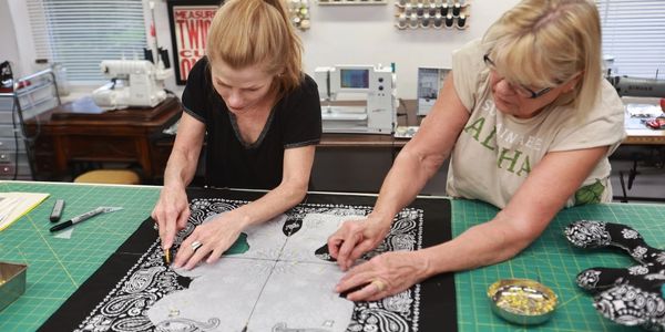 Two women handling teddy bear cutouts on a gridded mat.