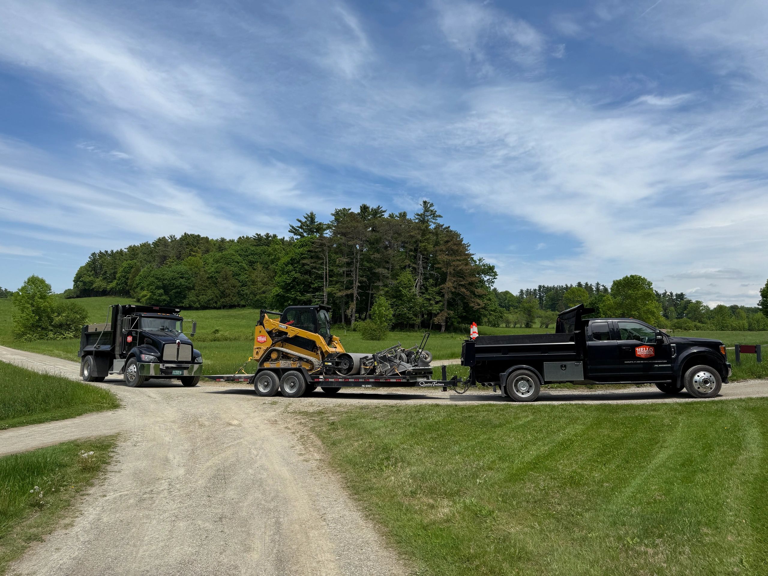 Two trucks and a yellow skid steer loader on a trailer in a rural setting.
