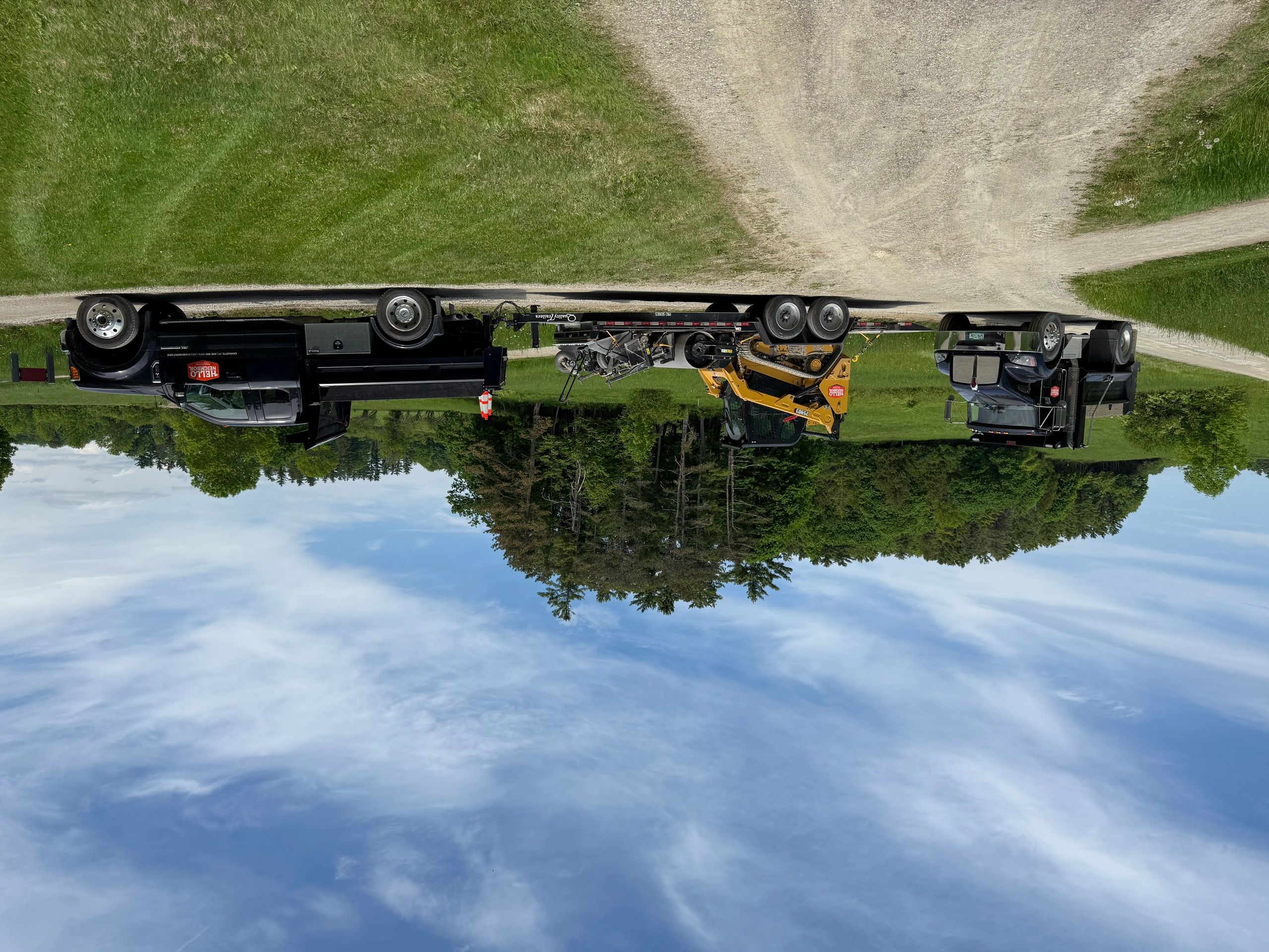 Two trucks and a yellow skid steer loader on a trailer in a rural setting.