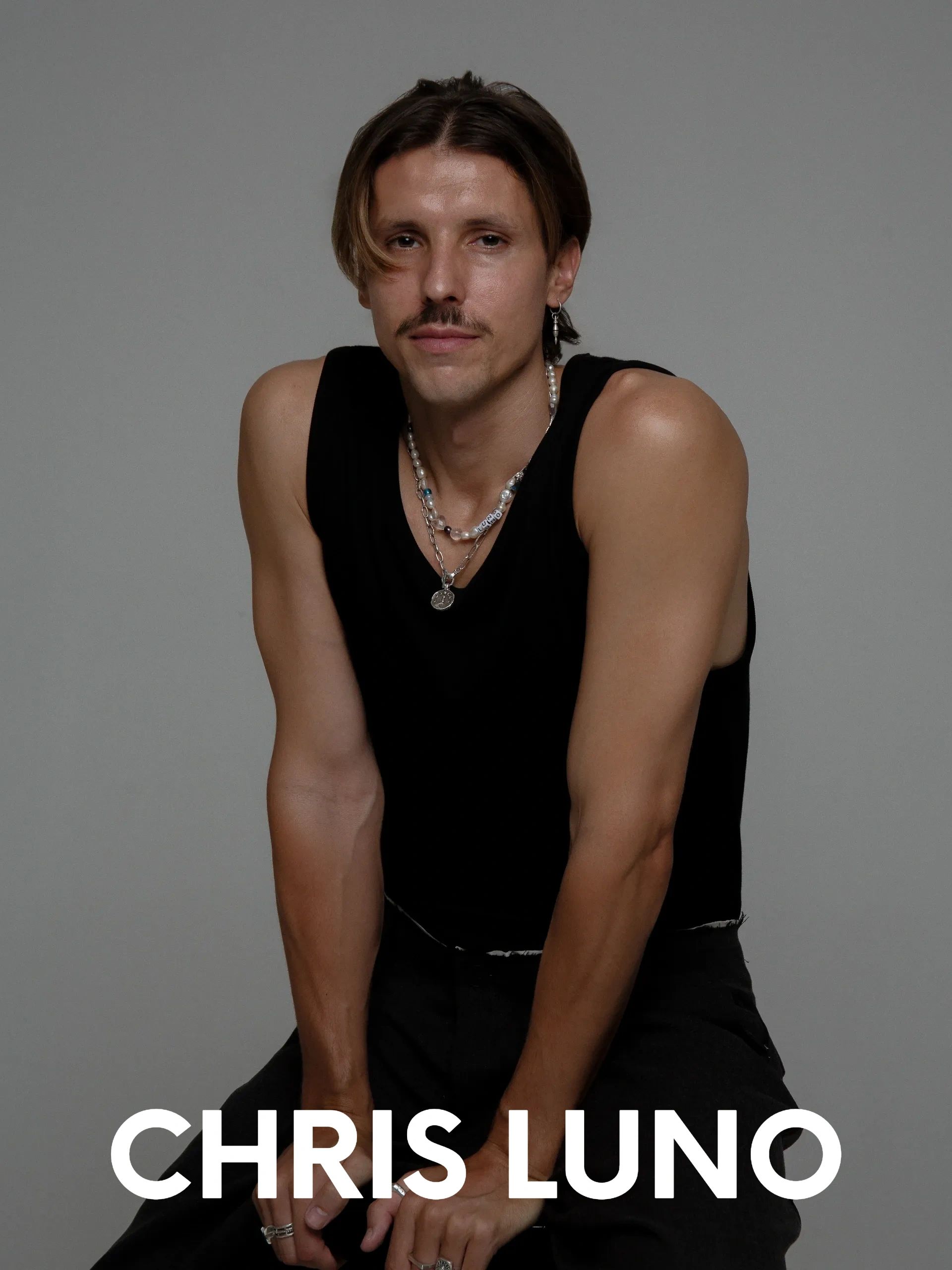 Portrait of Chris Luno in a black sleeveless shirt with a mustache and necklaces.