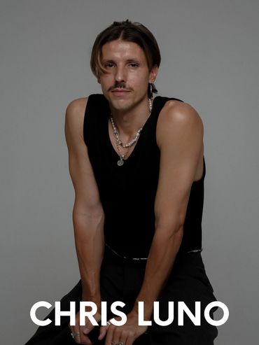 Portrait of Chris Luno in a black sleeveless shirt with a mustache and necklaces.