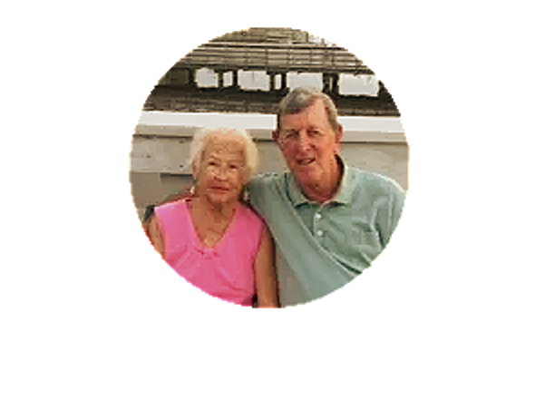 Elderly couple sitting together outdoors, smiling at the camera.