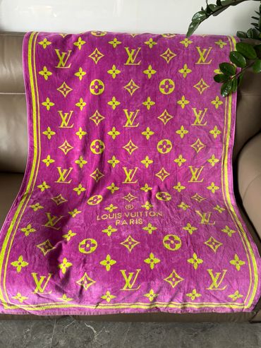 Pink and yellow Louis Vuitton blanket draped on a sofa.