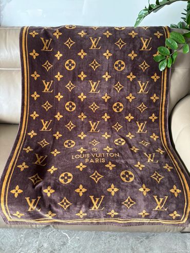 Brown Louis Vuitton blanket with iconic logo patterns draped on a sofa.