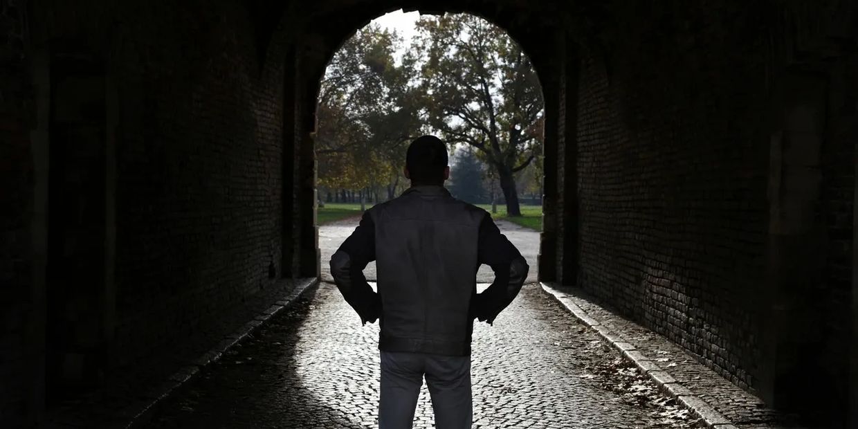 Person standing in a dark tunnel looking outside.