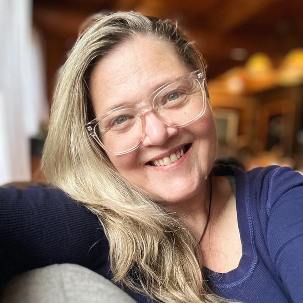 Smiling woman with clear glasses and long blonde hair.