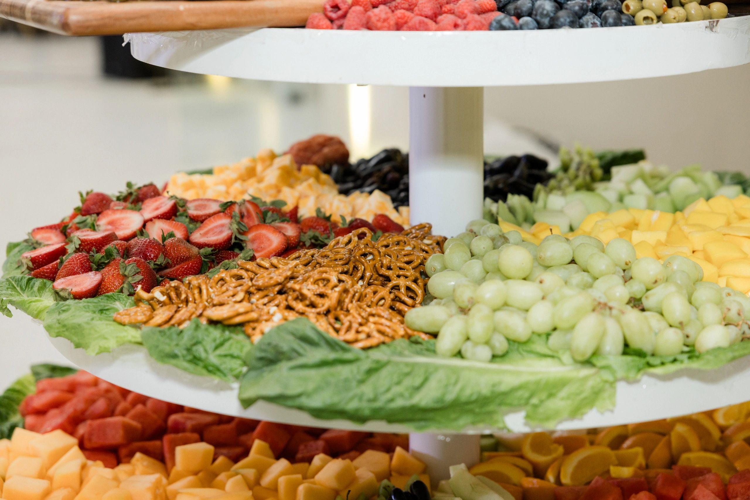 Two-tiered tray with strawberries, pretzels, grapes, cheese, and other snacks.