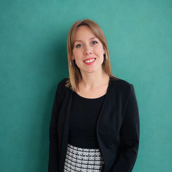 Femme souriante habillée en tenue professionnelle noire et jupe à motifs.