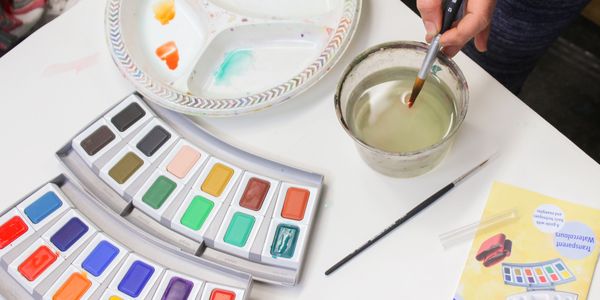 This is an overhead image of a student dipping her paintbrush in water and her paint palette.