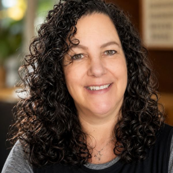 Smiling woman with curly dark hair in a warmly lit indoor setting.