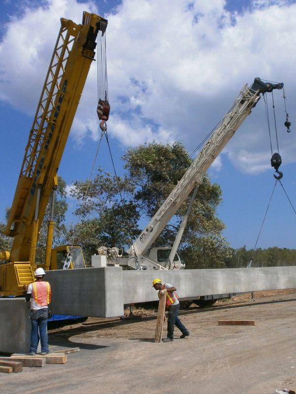 Dos grúas movilizan una viga de concreto en una obra.