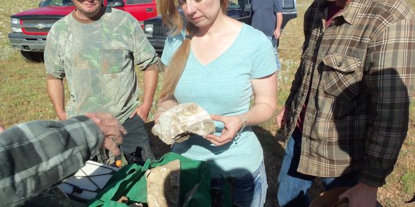 People outdoors examining large rocks on a sunny day.