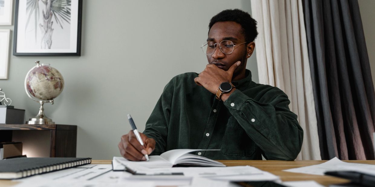 Young man writing and thinking at a desk.