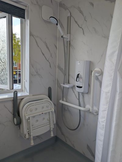 Accessible shower area with foldable seat and safety grab bars.