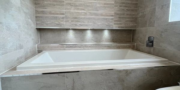 Modern bathtub with stone tile walls and recessed lighting.