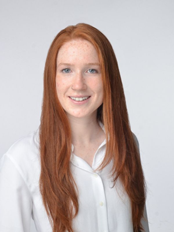 Young woman with long red hair and white shirt smiling.