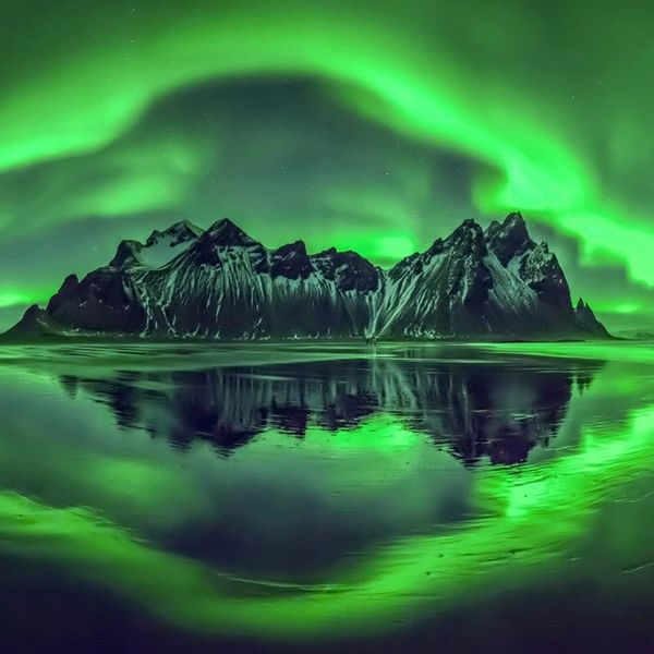 Image of rocky island in the Northern sea. Emerald green aurora Borealis above and reflected on the 