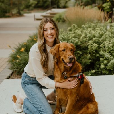 Woman kneeling next to her golden retriever dog outdoors.