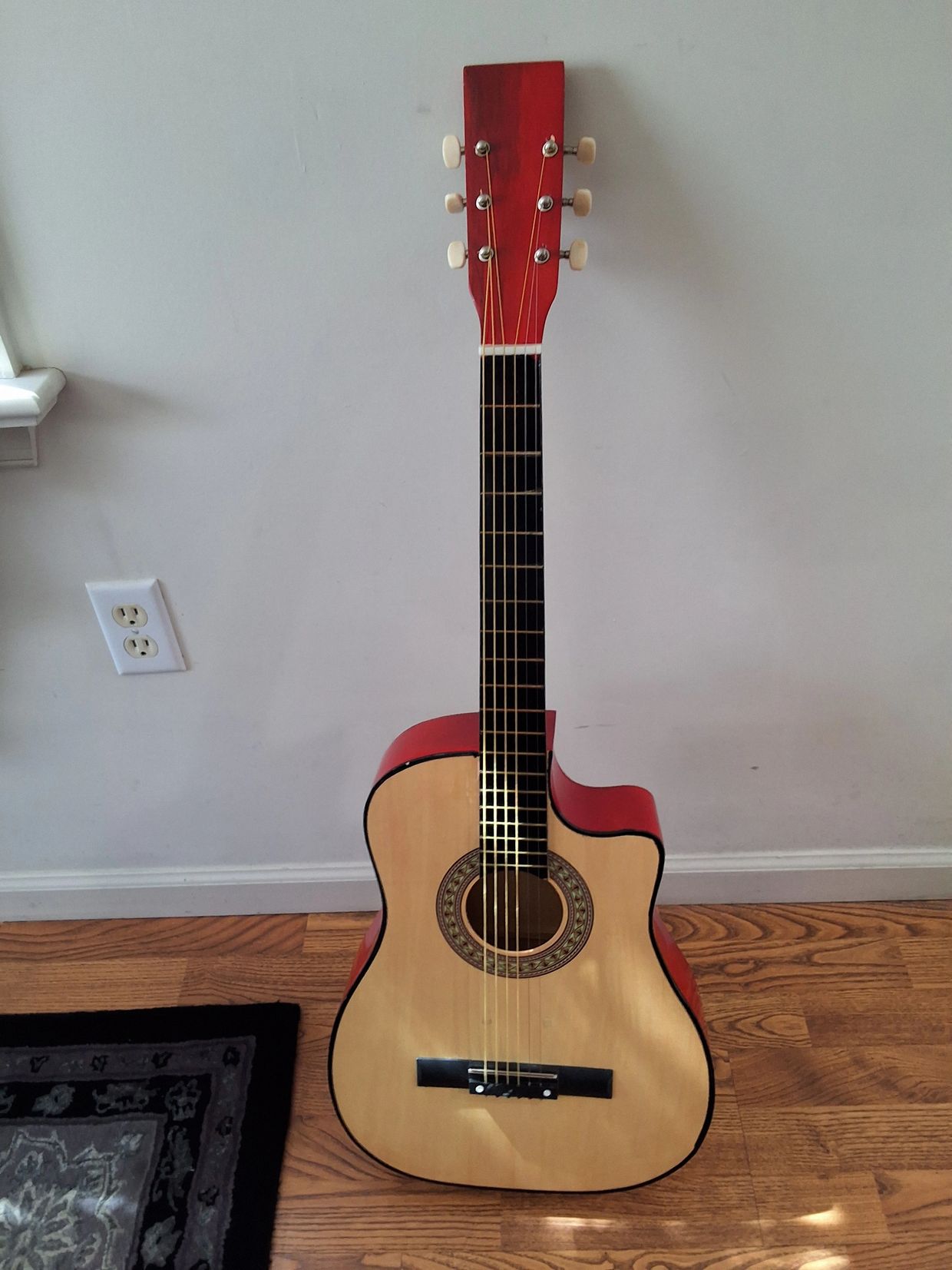 Acoustic guitar with a natural wood front and red sides and headstock.