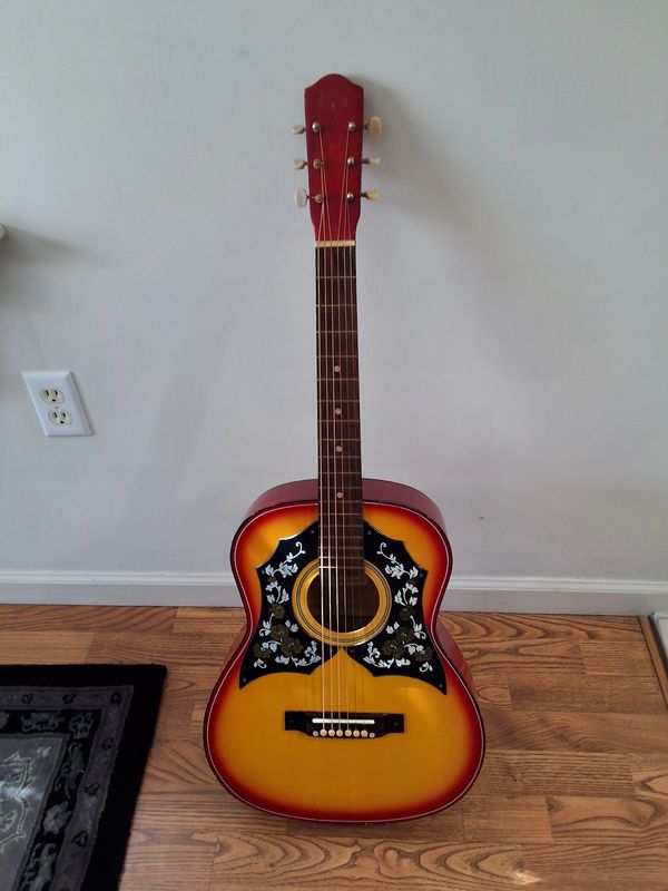 Vintage acoustic guitar with floral pickguard on wooden floor.
