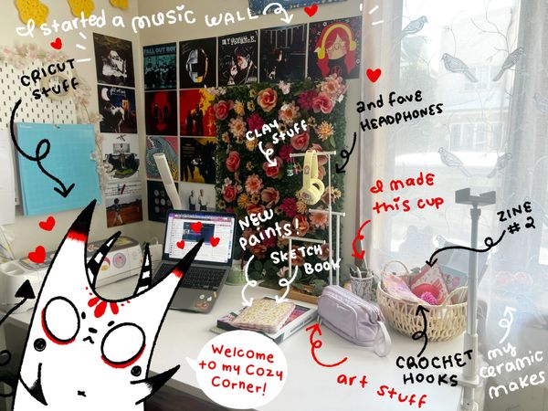 White desk with laptop, decorated with illustrated doodles and white imp character with horns.