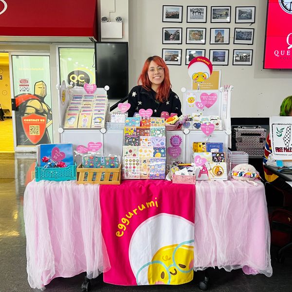 Smiling vendor at colorful egg-themed craft booth with stickers and accessories.