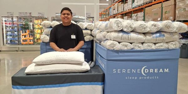 A smiling employee sits behind pillows at a Serene Dream sleep products display.