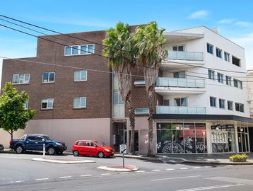 Modern mixed-use building with palm trees and parked cars on a city street.
