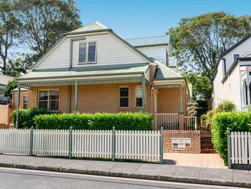 Two-story house with brick lower walls and white picket fence.