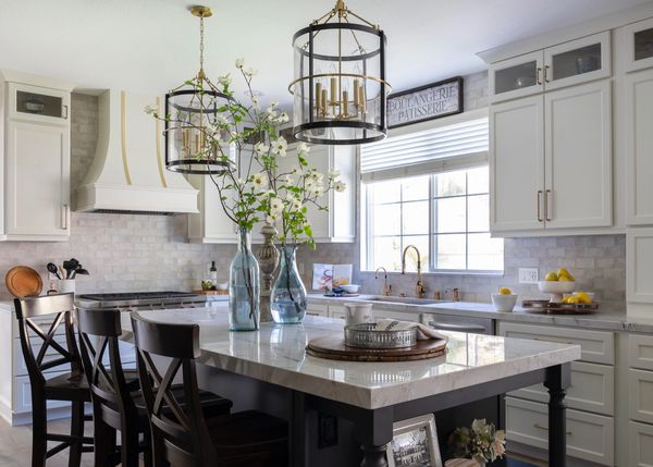 White and brass hood over cooktop with long island and pendant lights above