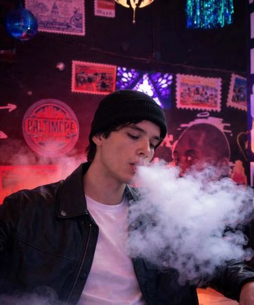 Young man in a beanie blowing smoke in a dimly lit room.