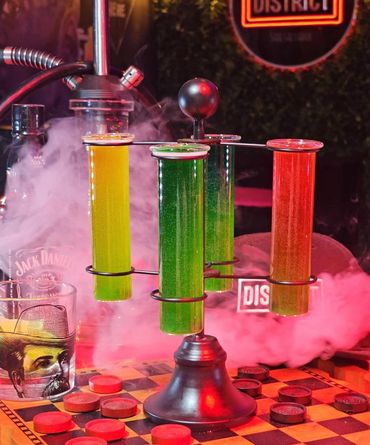 Colorful drinks in test tube holders with smoke in a bar setting.
