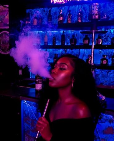 Woman exhaling smoke in a dimly lit bar with blue and purple lighting.