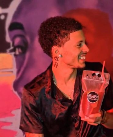 A man smiling while holding a drink in a vibrant, colorful setting.