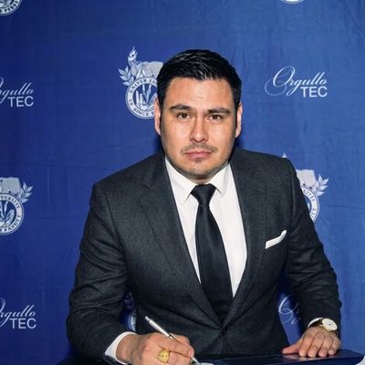 Man in a suit signing a document with a blue backdrop.